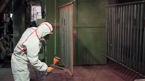 Powder coating of metal parts. Worker in protective suit sprays powder paint from gun on metal products
