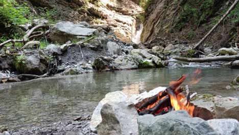 bonfire is burning peacefully in nature with no people around, surrounded by river and waterfall