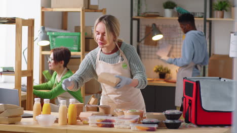 female worker packing meal boxes and drinks in food delivery bag