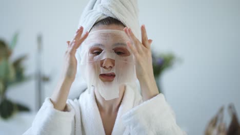 Porträt-Einer-Jungen-Hausfrau,-Die-Im-Badezimmer-Eine-Gewebe-Gesichtsmaske-Zur-Hautpflege-Aufträgt