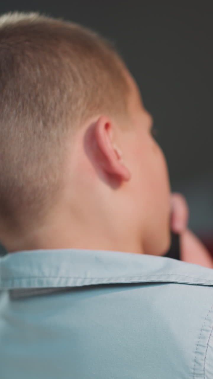Schoolboy calls to mother on smartphone turning head to side on blurred background. Boy with short haircut sits at home waiting for answer on phone call closeup