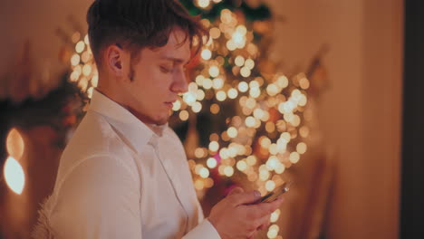 man using smartphone at illuminated home during christmas