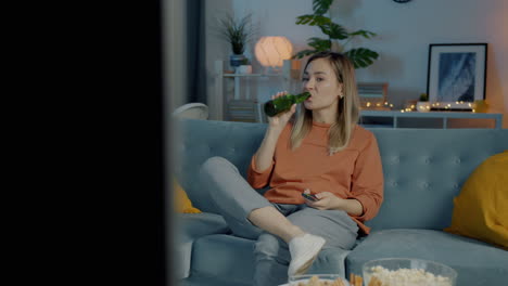 woman relaxing on couch, watching tv and drinking beer