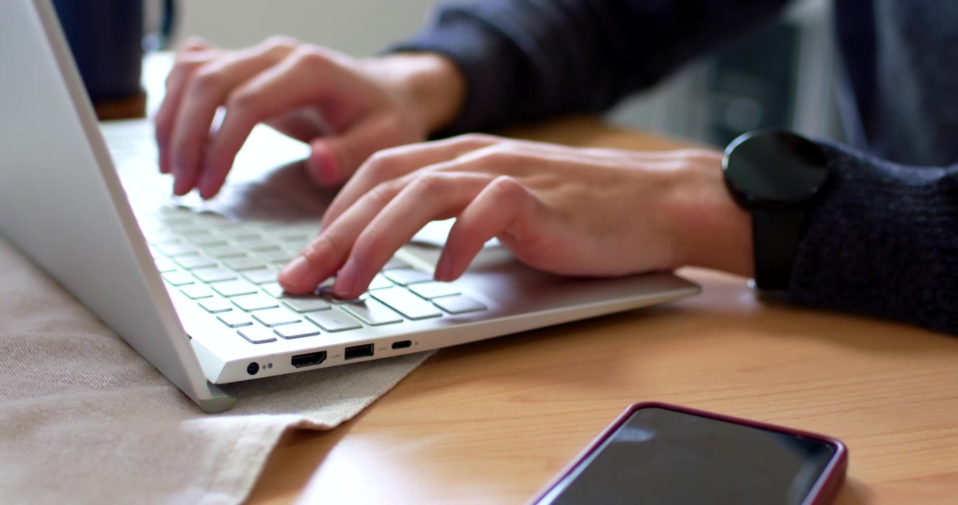 Uomo afroamericano che digita con le mani posate sopra la tastiera su un tavolo di legno, lavorando al laptop