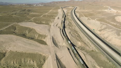 long cargo train traveling through nevada state next to vehicles driving on asphalt road in usa