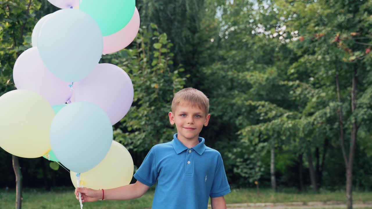 Child with balloons in his hands. Boy plays in the summer park. Spins around itself
