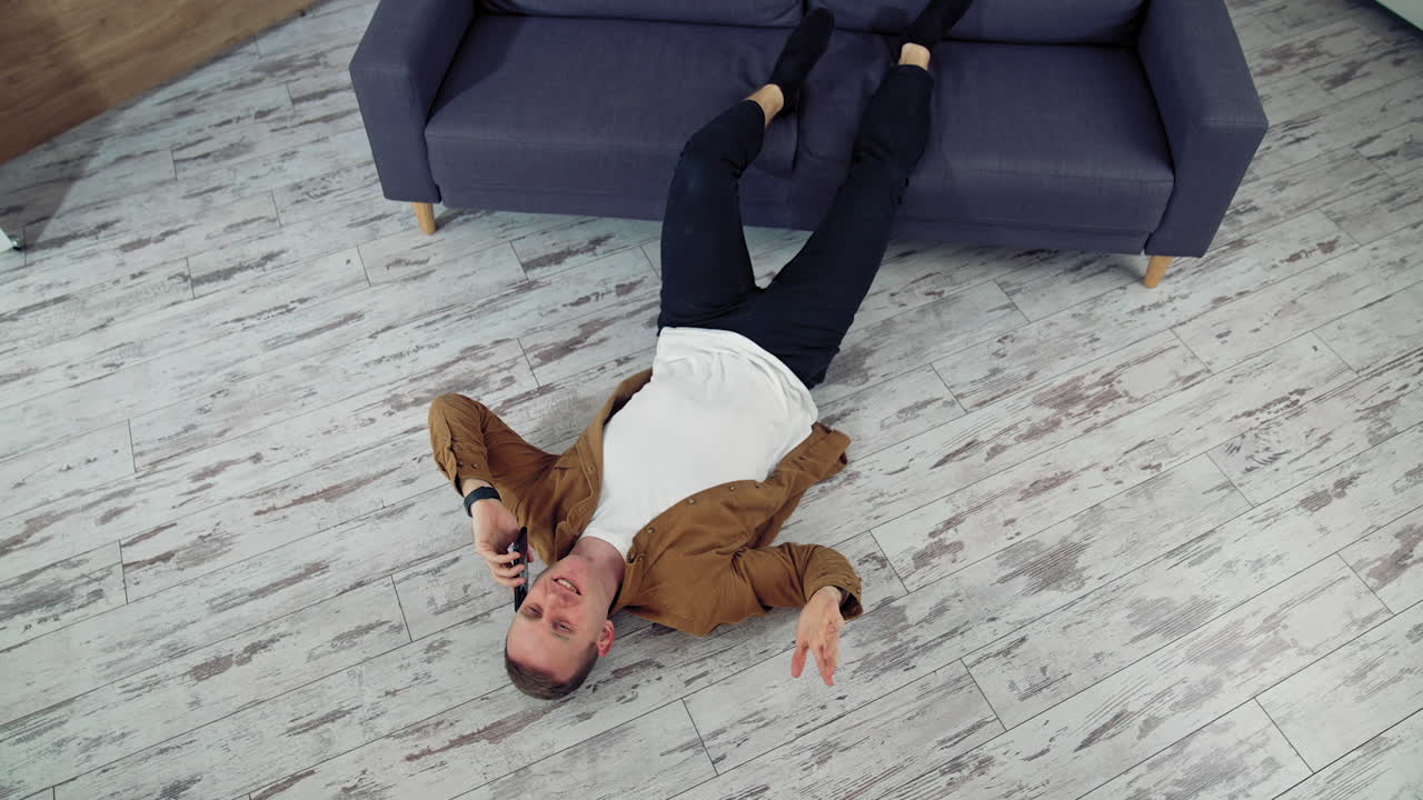 Young man speaking the phone at home. Tired man working through the phone while lying on a floor. Top view.