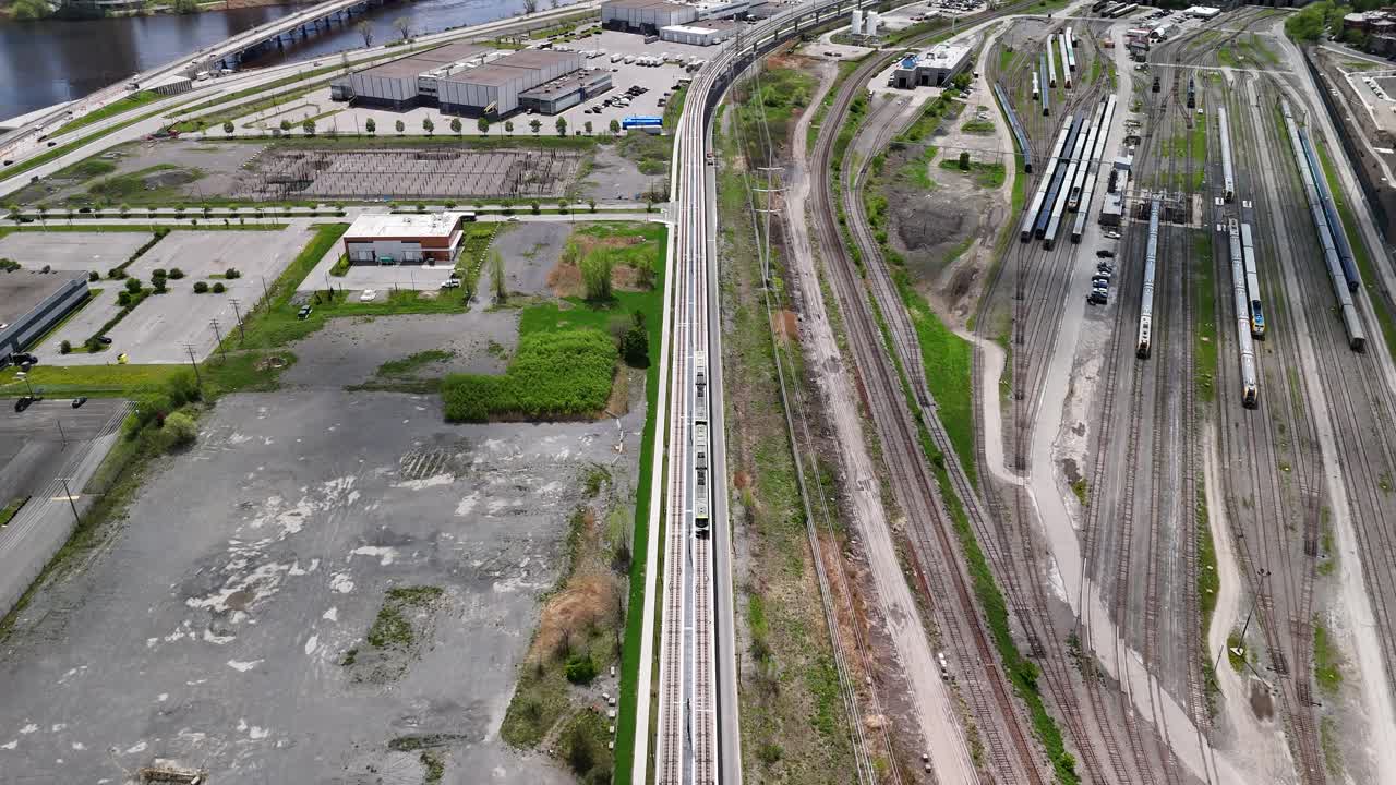 Overhead shot of REM train travelling down train tracks along side train yard, St Laurence River to the left, urban setting.