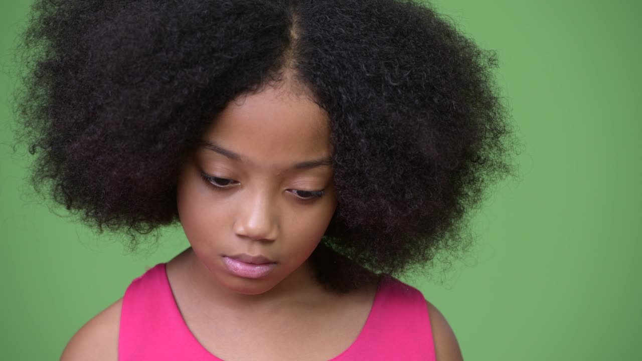 Giovane e triste ragazza africana con capelli afro che pensa mentre guarda in basso.