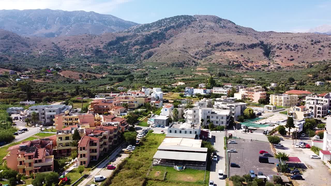 Cinematic aerial view of township and mountain range in background in Crete