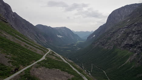 Aerial-shot,-panning-down-a-rocky-hillside,-over-the-serpentine-Trollstigen-mountain-road-in-Norway