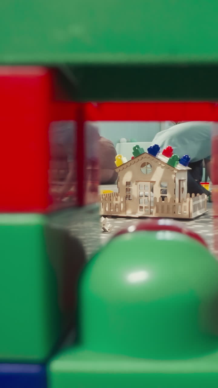 소녀는 아기 인형을 돌보는 동안 금발 소년은 건물 블록을 짓습니다. 아이들은 반사 빛의 전망으로 바닥에 앉아 큐브에 건설 된 벽에서 클리어런스를 통해 볼 수 있습니다.