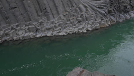 bubbles in green water river flowing between twisted basalt columns