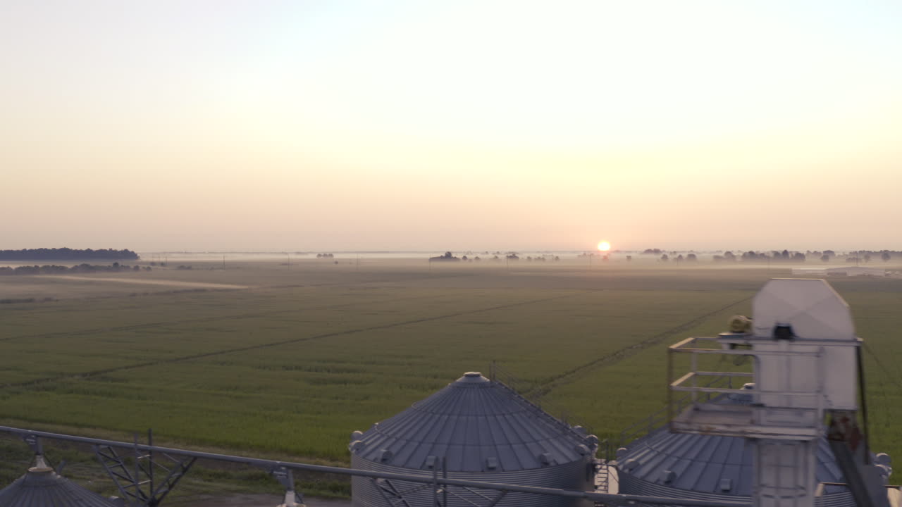 The sun rises over rural farmland in Missouri with silos in the foreground.