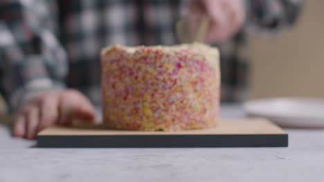 close up shot of person at home cutting slice from rainbow celebration cake on table