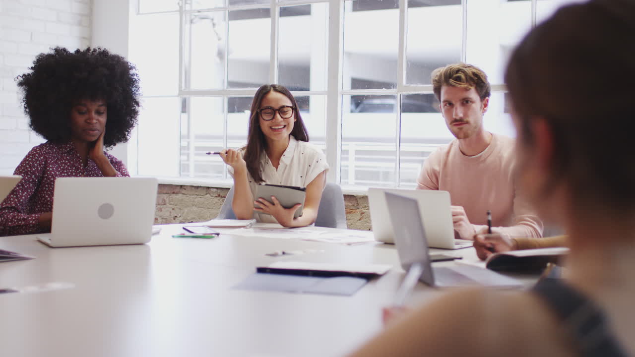 Millennial creative coworkers in discussion around a table in a meeting room, selective focus