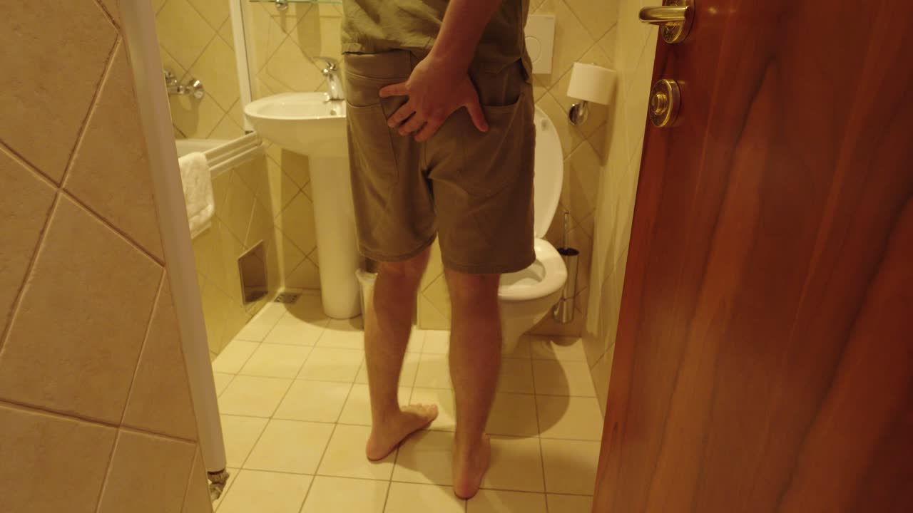A man in casual clothes rushes towards the bathroom, holding his backside in urgency. Typical gesture illustrates stomach pain, diarrhea or sudden need for toilet