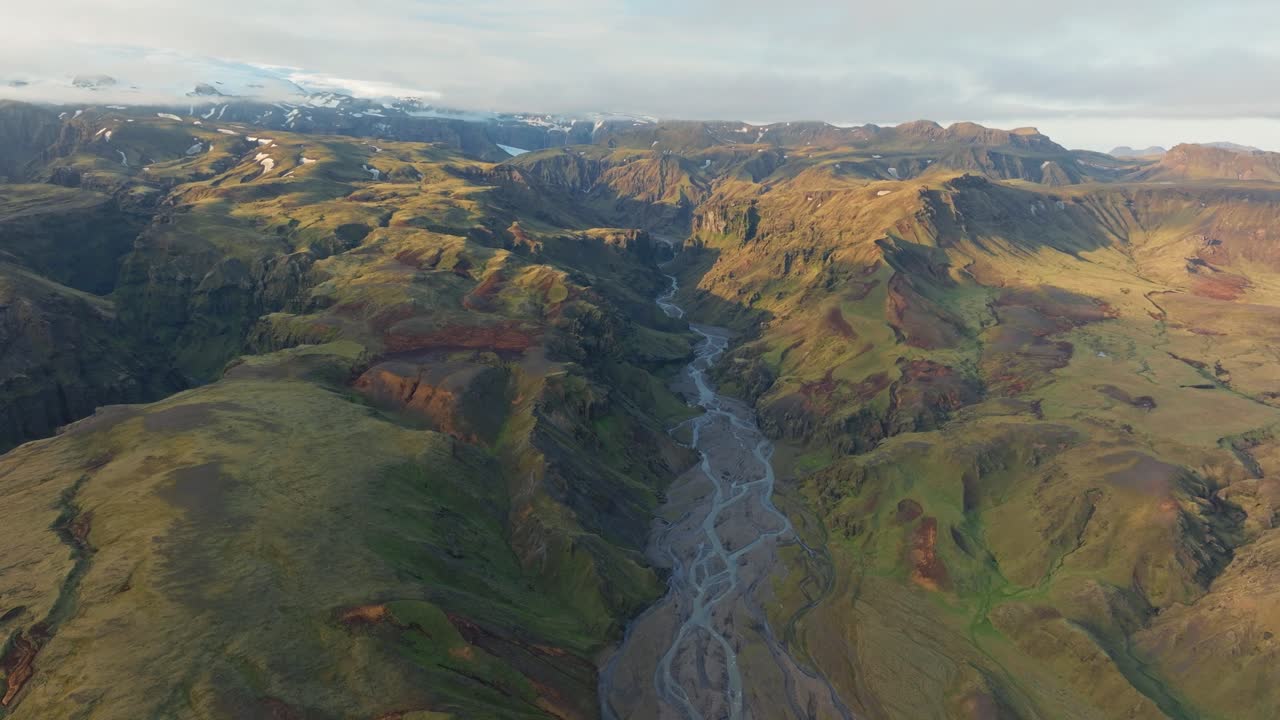 Aerial view of a stunning braided river valley near Hafursey, Iceland, surrounded by rugged volcanic mountains and glacial formations.