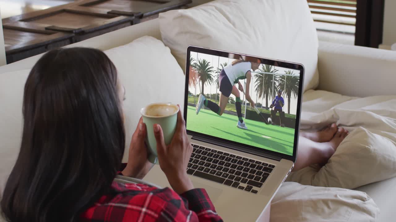 Composite of woman sitting at home holding coffee watching hockey match on laptop
