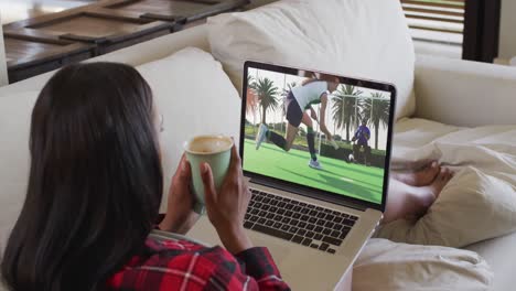 compuesto de una mujer sentada en casa sosteniendo un café viendo un partido de hockey en una computadora portátil