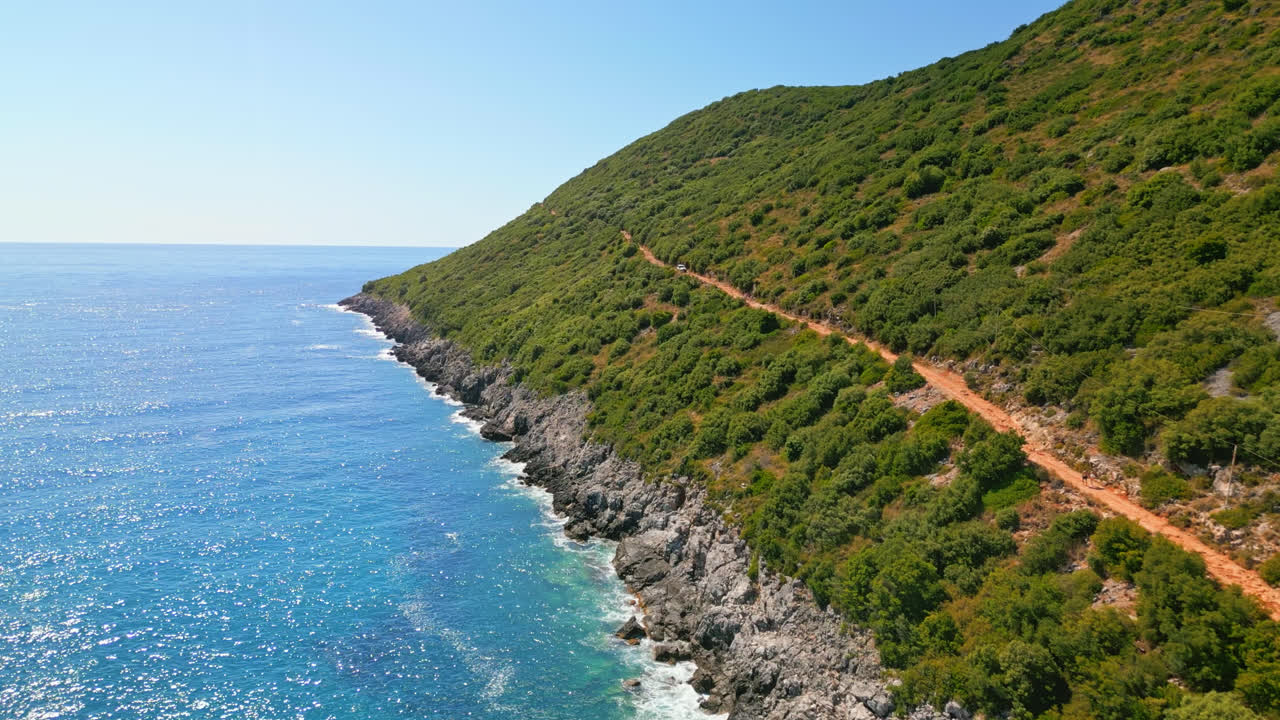 воздушный беспилотник вперед движется выстрел над пешеходной дорожкой на холме рядом с красивой голубой морской водой вдоль пляжа gjipe, албания в солнечный день