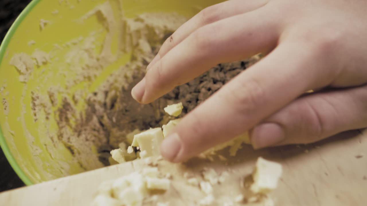 Slow Motion of female hands preparing chocolate cookies pushing the cut up chocolate into the bowl.