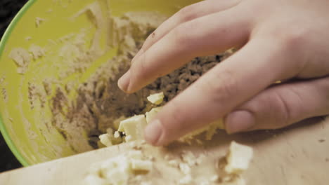 slow motion of female hands preparing chocolate cookies pushing the cut up chocolate into the bowl.