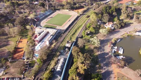 tren azul corriendo y cruzando el área de palermo con estanques y jardines de rosas en buenos aires, campo de fútbol en segundo plano