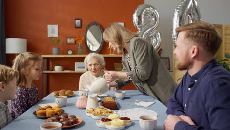 Woman Pouring Tea for Family Members at Grandma Birthday Dinner