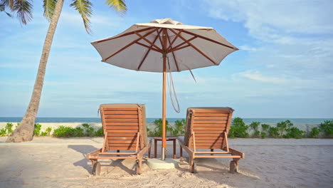 empty wooden lounges under a big white umbrella on a sandy beach near the ocean during a sunny bright day