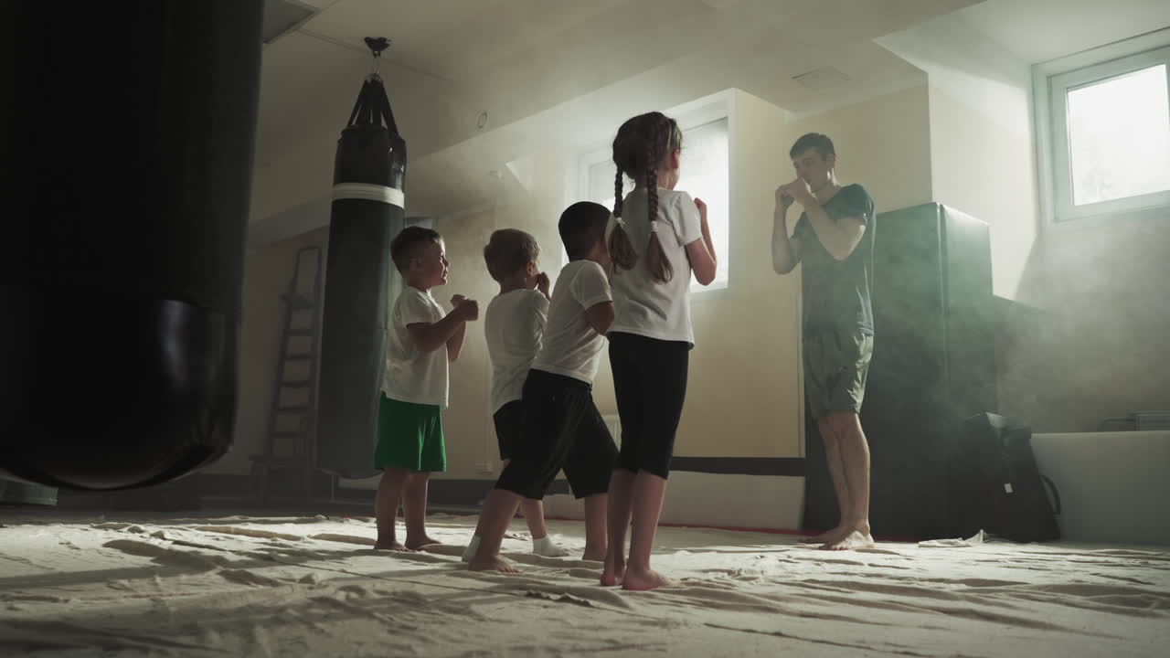los niños golpean el aire siguiendo al entrenador en la clase de artes marciales. los deportistas junior estudian atacar con las manos con el maestro en el gimnasio en cámara lenta. niños sanos