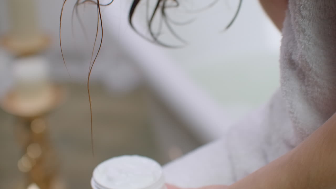 красивая молодая женщина в полотенце для ванны наносит лосьон на плечи и улыбается, стоя в ванной