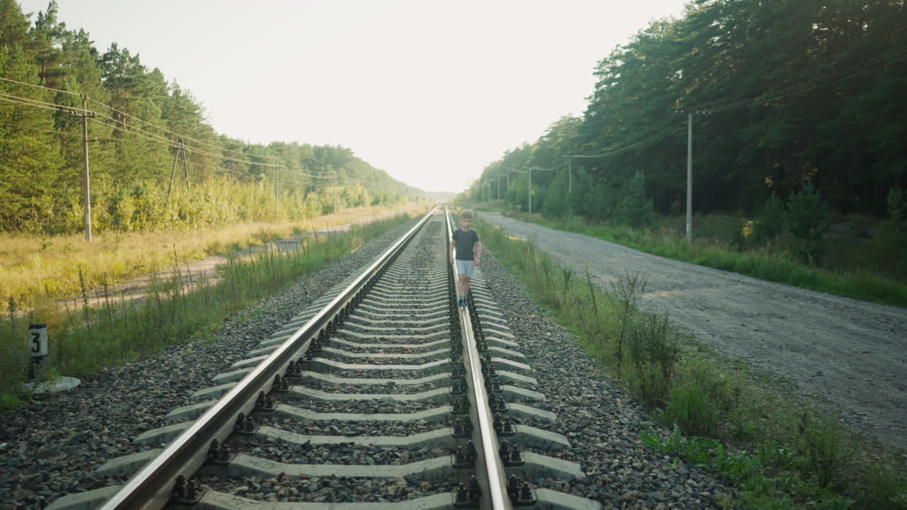 kid in casual outfit walking straight on railway beam, surrounded by trees and power lines, open sky above and gravel tracks below, in a quiet countryside setting with soft natural sunlight