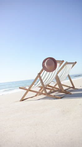 vertical video: beach scene with two empty lounge chairs and hat, relaxing by sea