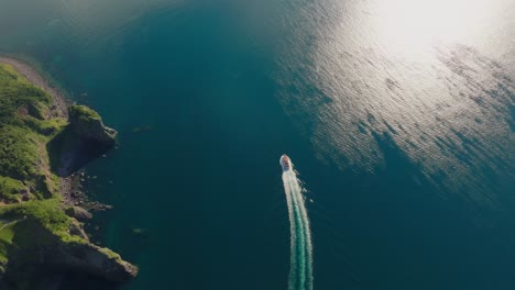 aerial tilts up motorboat sail in calm japanese sea at shiretoko hokkaido national park, wide natural view under sunlight