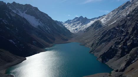 Dolly-in-aerial-view-of-Laguna-del-Inca,-surrounded-by-snowcapped-mountains,-Los-Andes,-Chile