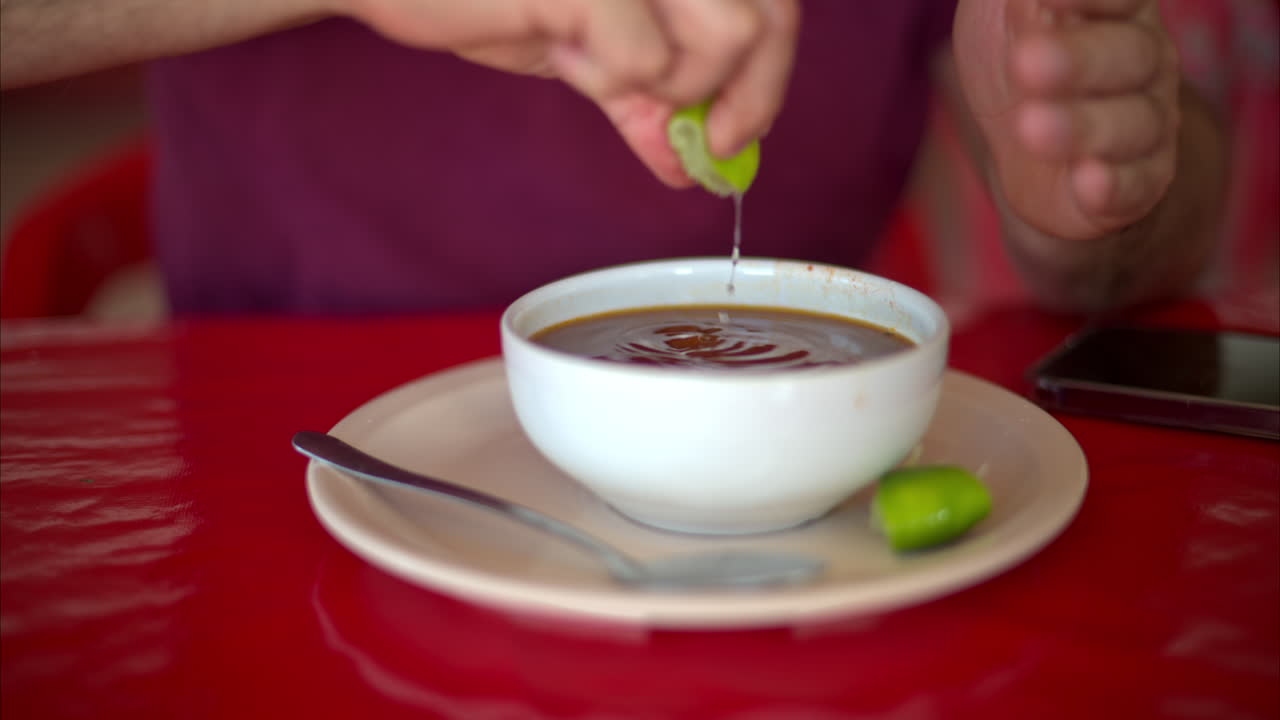 Close up slow motion of a Latin man squeezing lime into his barbacoa broth in a restaurant in Mexico