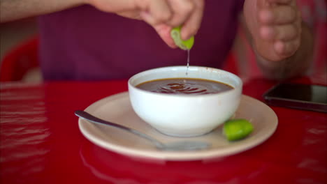 Nahaufnahme-Zeitlupe-Eines-Lateinischen-Mannes,-Der-In-Einem-Restaurant-In-Mexiko-Limette-In-Seine-Barbacoa-Brühe-Drückt