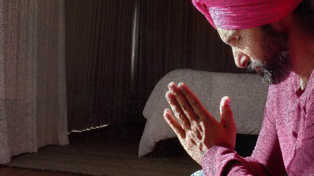 Man with turban sitting by lace curtains, holding palms, sunlight shifting supporting health