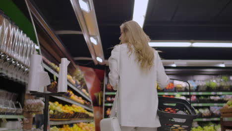 view back girl walking through the supermarket with a basket in his hands considering the shelves of fruit