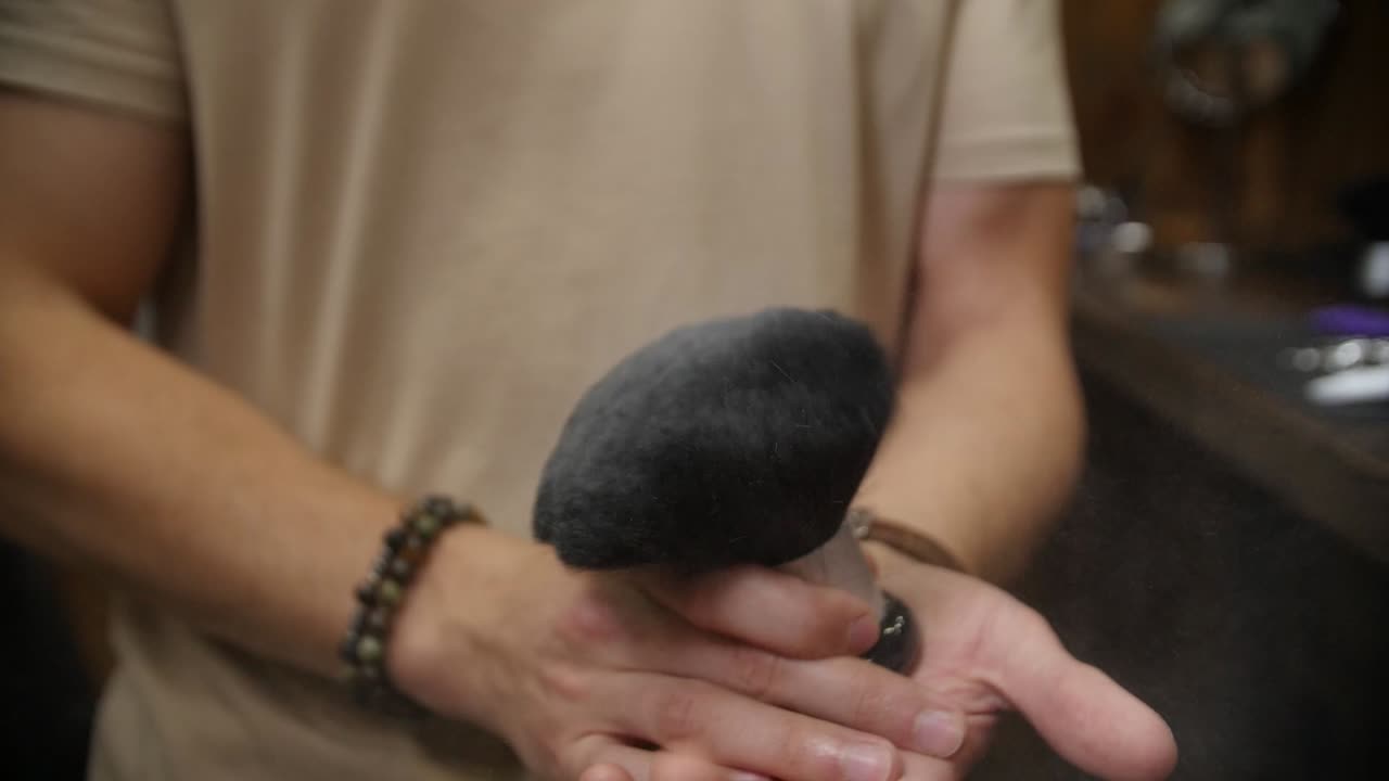 el peluquero rocía el cepillo para el cabello con polvo y lo golpea con las manos