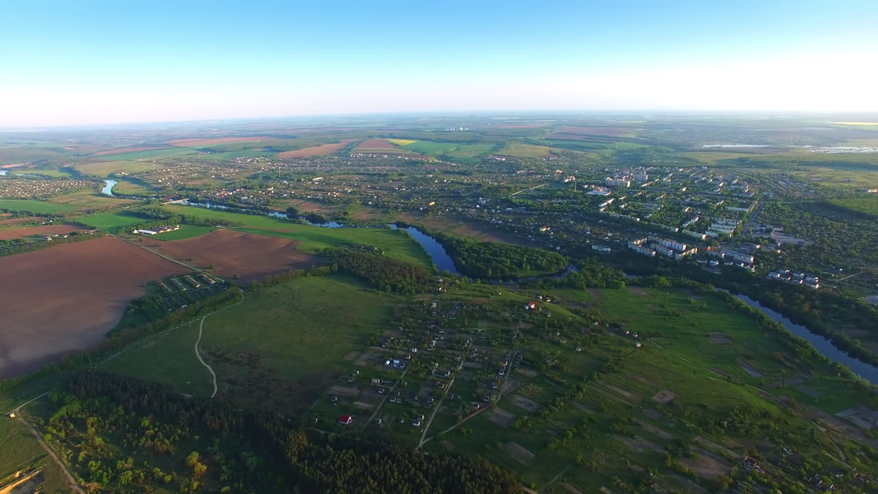 Vast scenic view of urban area and suburbs on sunny day. Wavy river crossing the green landscape. City dwelling around water artery. Top view.