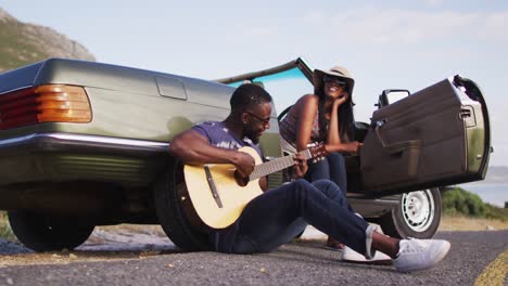 hombre afroamericano tocando la guitarra para su novia mientras estaba sentado en la carretera