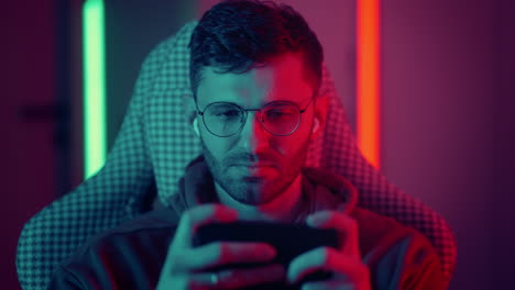 feliz jugador usar auriculares competición jugar videojuego en línea con teléfono inteligente coloridas luces de neón en la sala de estar en casa. esport juego de transmisión en línea casa concepto de actividad de cuarentena. imágenes de alta calidad 4k