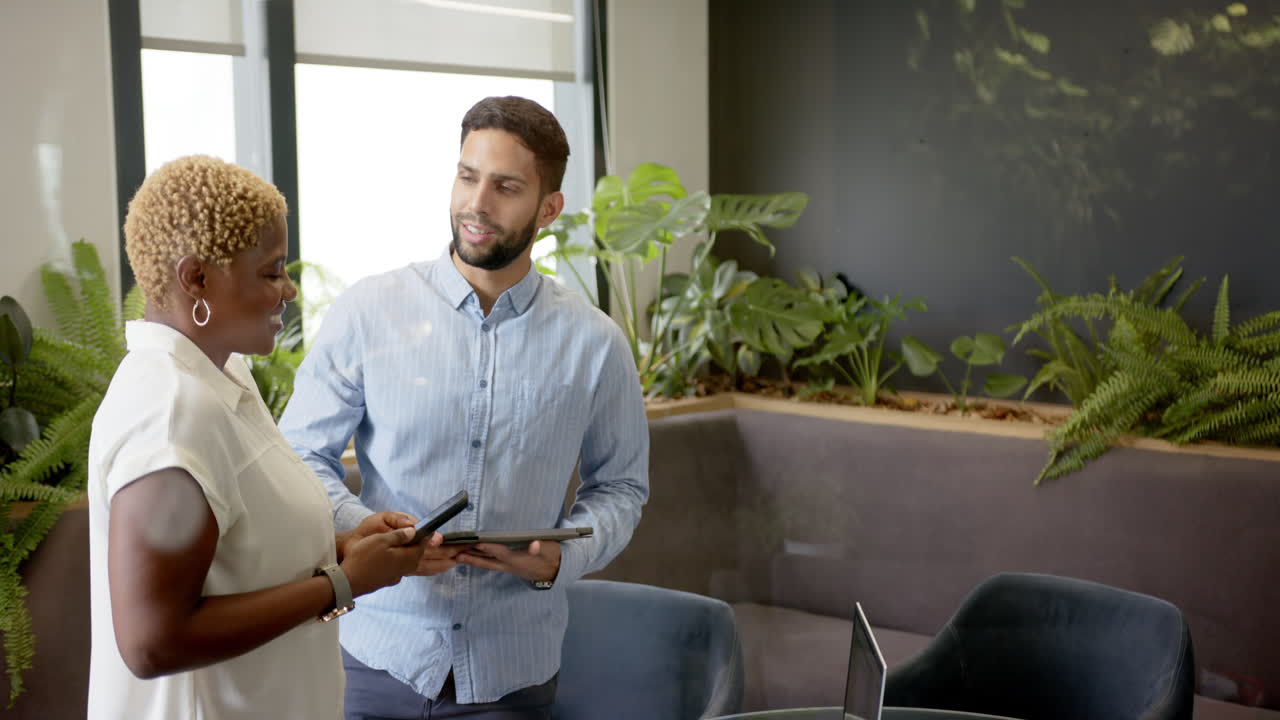 Smiling diverse colleagues holding tablets in modern office with indoor plants, copy space
