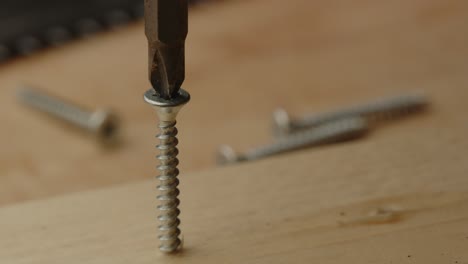 close up of drill bit of electronic screwdriver being placed in screw and drilling it into wooden board in slow motion