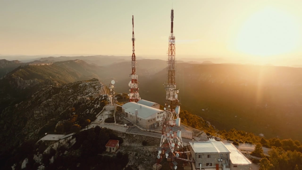 Riprese cinematografiche 4K con drone che orbita attorno a torri di telecomunicazione montane all'alba, sopra creste forestali e valli remote. Paesaggio aereo suggestivo con antenne di trasmissione, natura selvaggia e infrastrutture.