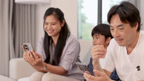 a family of three sits on a sofa, engaging with a smartphone in a bright, cozy living room