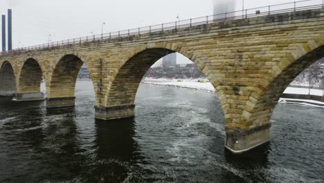 drone flies between famous stone arch bridge in downtown minneapolis in winter