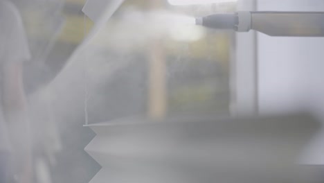 close-up of an industrial machine slowly spraying transparent vapor onto an unrecognizable surface in a documentary-style handheld shot